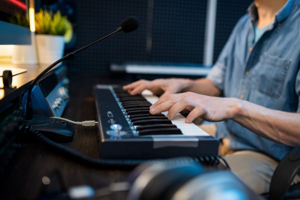 Young male musician touching keys of piano keyboard while sitting by workplace